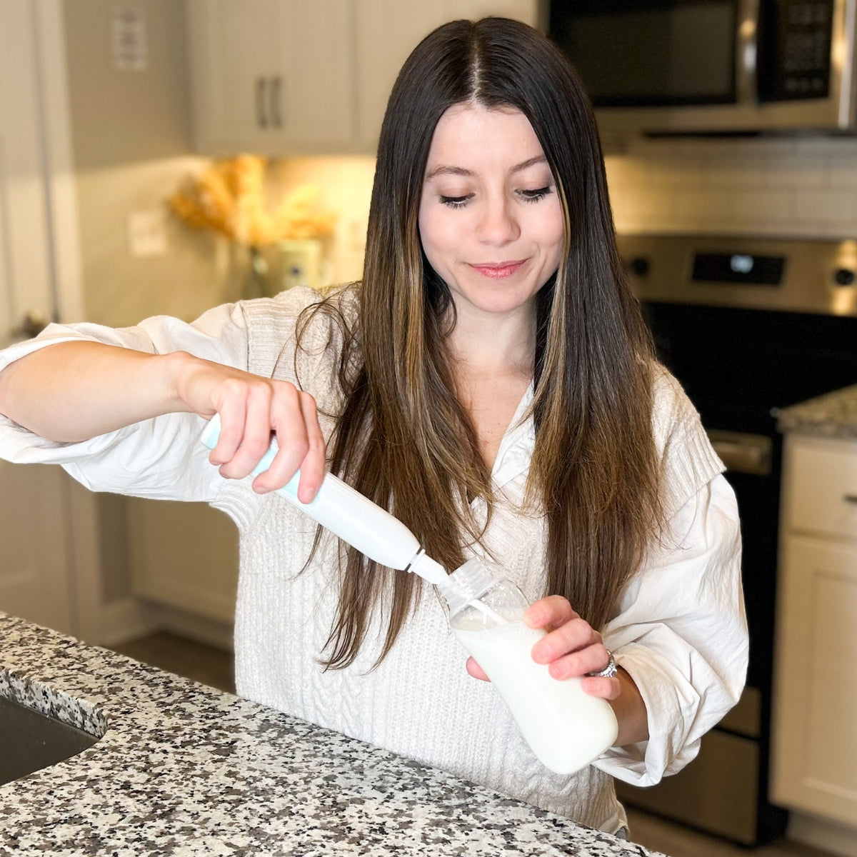 A woman is using a MomMed electric bottle brush to clean her baby's baby bottle.