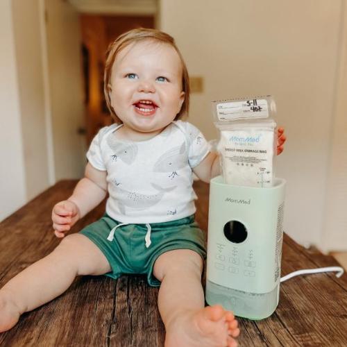 The baby happily takes a photo with the MomMed baby bottle warmer